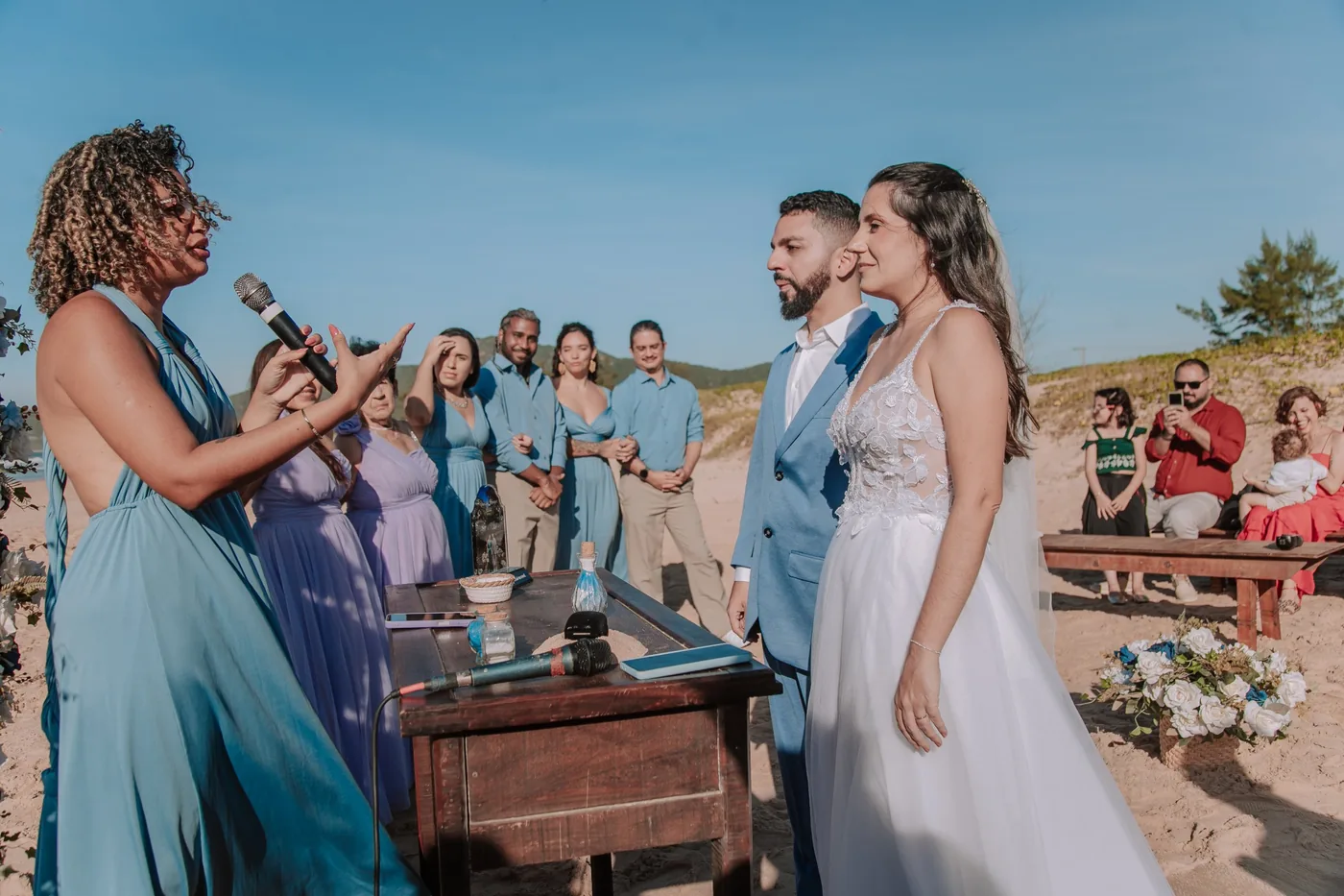 Fabiana conduzindo a cerimônia diante dos noivos, com o altar de areia ao centro
