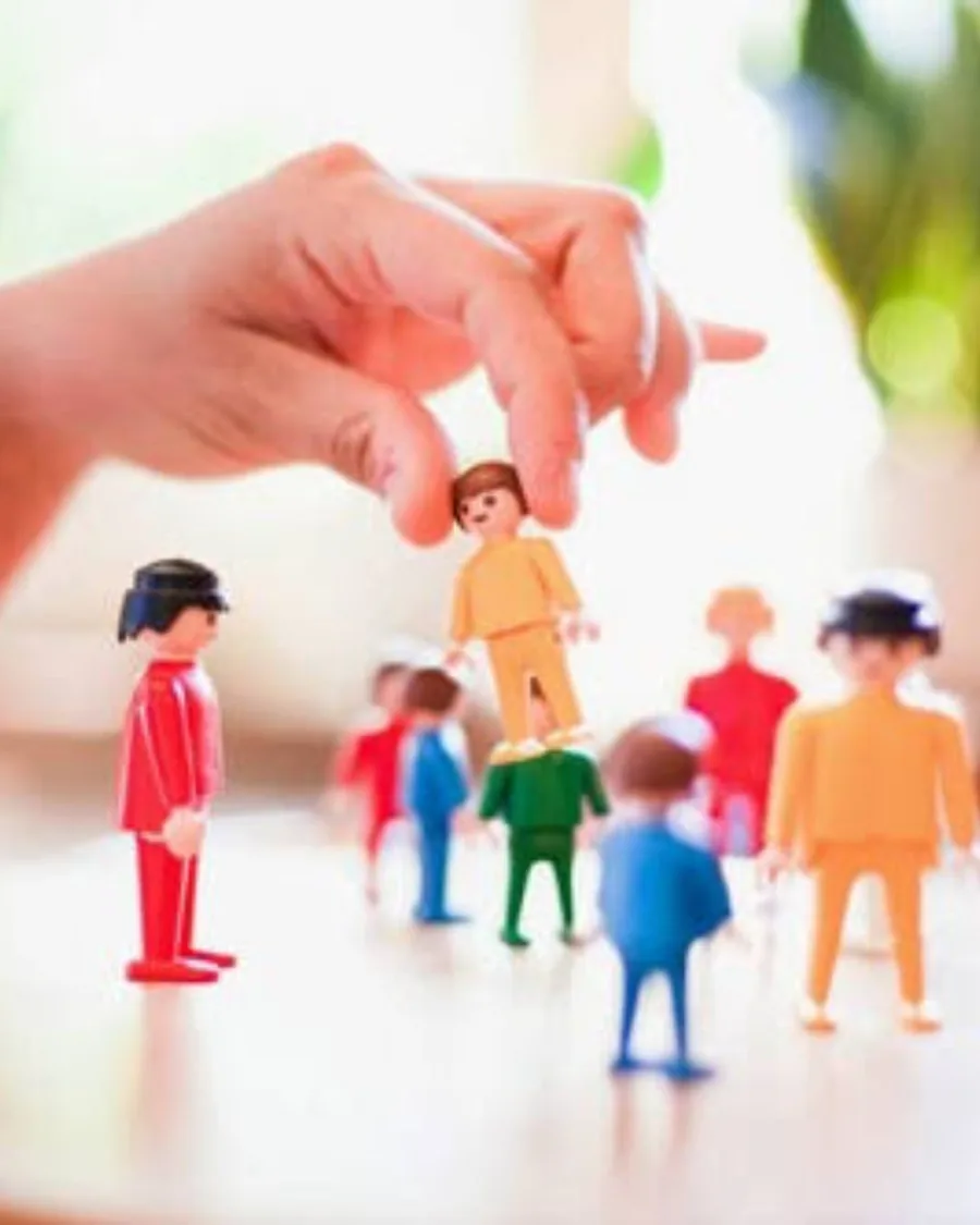 Mão posicionando um boneco entre vários outros, representando uma constelação familiar